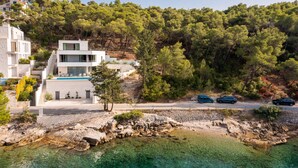 A modern villa with a pool, located on a rocky coastline with clear waters and dense forest in the background. - Beachfront Villa Charisma with Pool (Splitska)