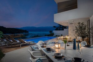 Un área de comedor al aire libre y moderna con piscina, con vistas a un paisaje montañoso.