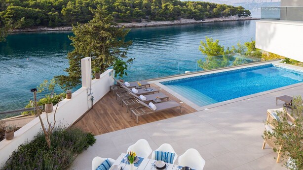 A modern outdoor pool area with a dining setup overlooking a lake and forested hills. - Beachfront Villa Charisma with Pool (Splitska)
