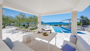 A covered outdoor area with a pool, seating, and a table with fruit and a bottle. - Villa Auras with Heated Pool (Slano)