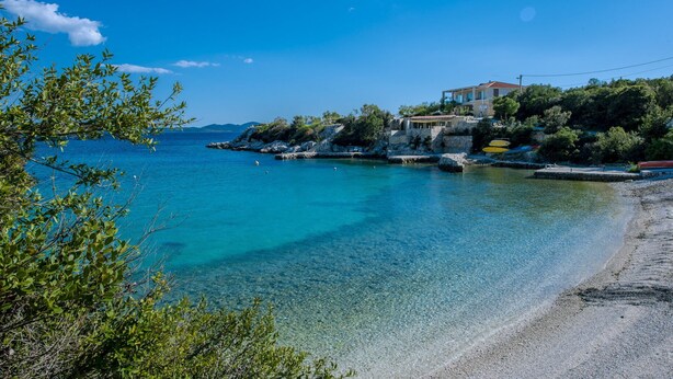 A coastal scene with a clear blue sea, a rocky shoreline, and a building with a red roof. - Villa Auras with Heated Pool (Slano)