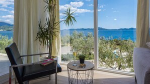 A room with a large window overlooking a coastal view, a chair, a small round table with a glass of wine, and a potted plant. - Villa Auras with Heated Pool (Slano)