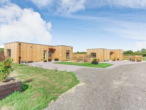 Een modern gebouw met een houten gevel, een grindpad en een gazon met potplanten.