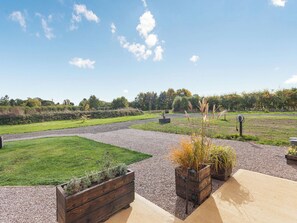 Un espace extérieur aménagé avec un chemin de gravier, des jardinières en bois plantées et un terrain herbeux.