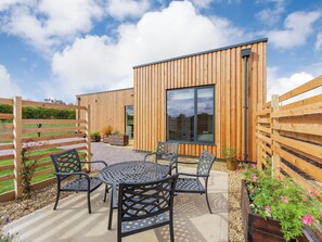 Een modern houten gebouw met een terras, inclusief een ronde tafel en stoelen.