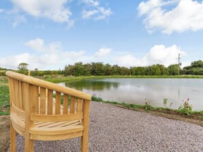 Un banc en bois, placé face à un étang, avec un chemin de gravier et de la verdure en arrière-plan.