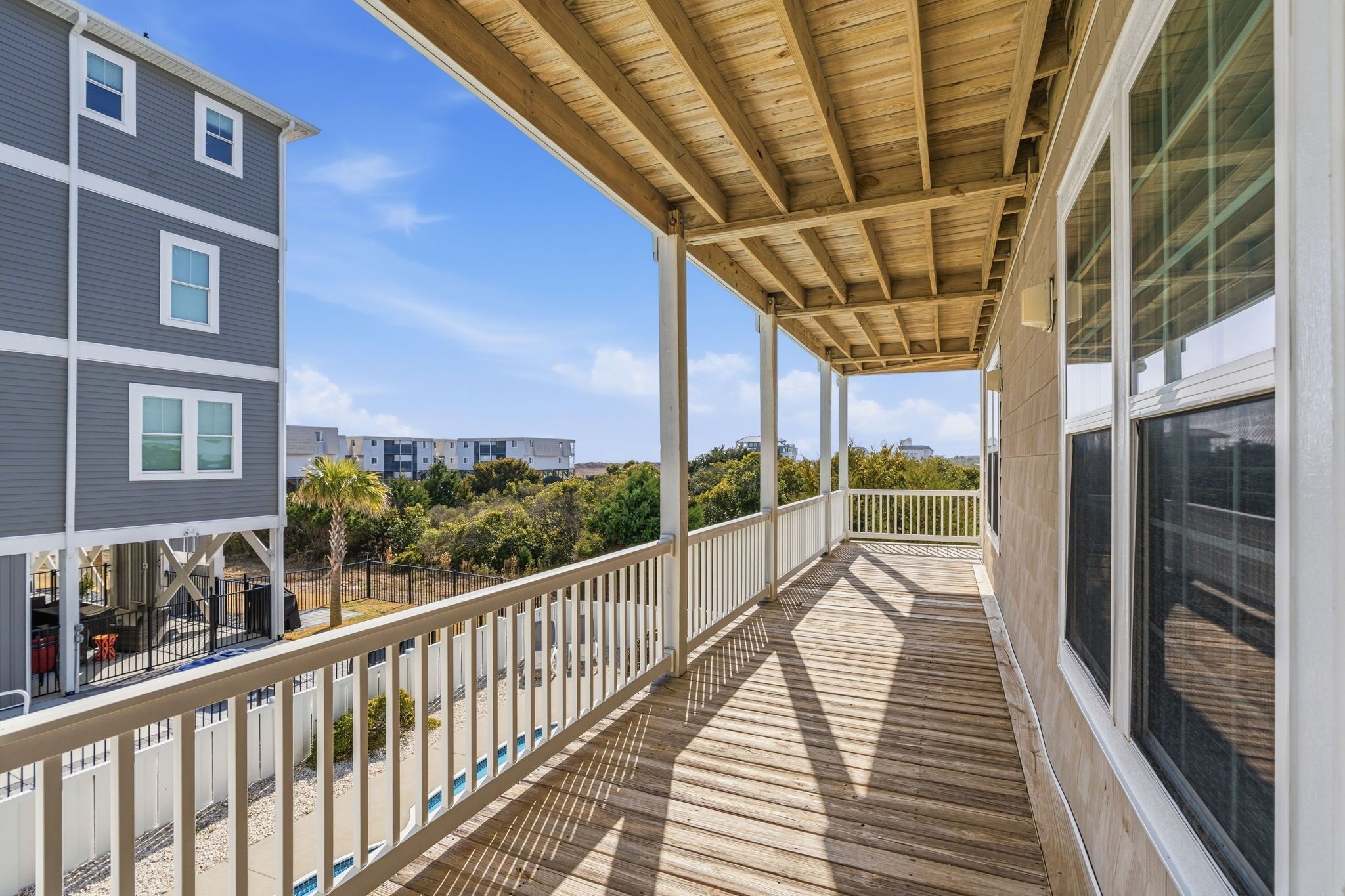 A wooden deck with railings, a covered area, and a view of neighboring buildings and greenery.