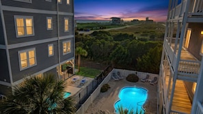 A multi-story hotel with a swimming pool, outdoor seating, and a view of the ocean at sunset.