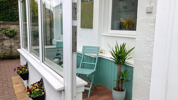 A white exterior with a window, a teal chair, and a potted plant.