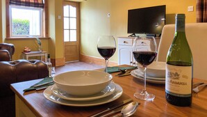 A dining area with a wooden table set for two, two wine glasses, a bottle of wine, and a bowl.