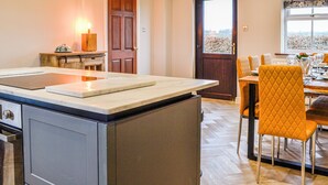 A modern kitchen with an island, a dining area with yellow chairs, and a large window with a view. - 4 bedroom accommodation in Carlisle (Carlisle)