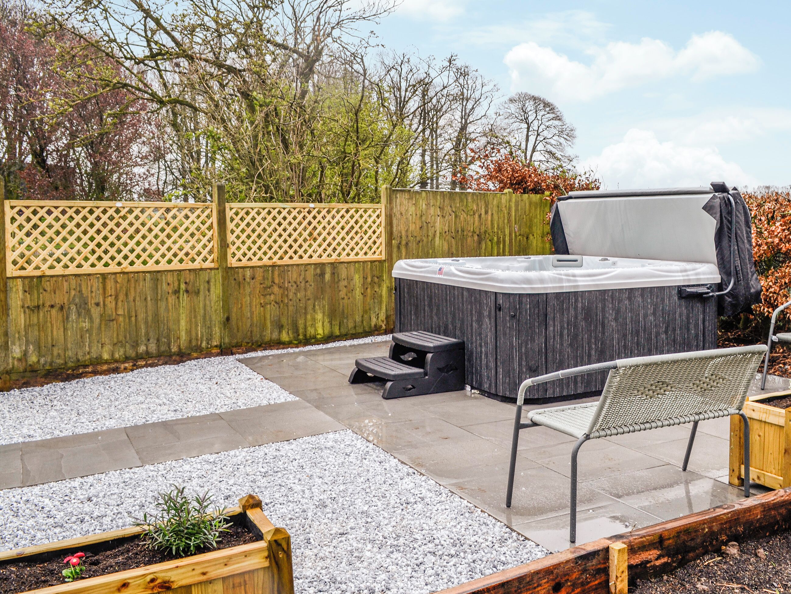 Un bain à remous dans un jardin, avec une clôture en bois, un banc et un petit tabouret.