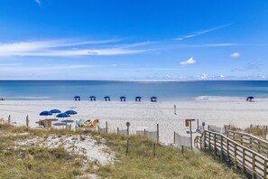 A beach with a wooden boardwalk leading to beach umbrellas and a lifeguard tower. - Windancer 212. Gulf Front End Unit, Free Beach Service, Heated Pool. (Miramar Beach)