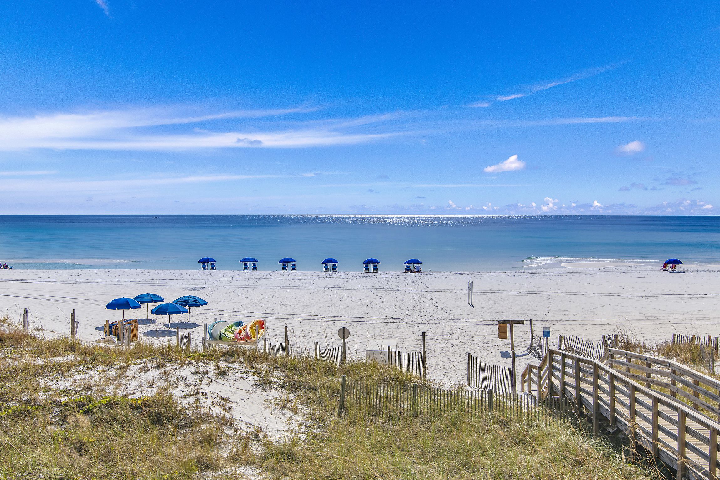 A beach with a wooden boardwalk leading to beach umbrellas and a lifeguard tower.