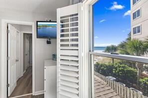 Une pièce dotée d’une grande fenêtre donnant sur une plage, d’un téléviseur fixé au mur et d’une porte blanche menant à une autre pièce.
