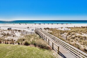 Une plage avec une promenade en bois menant au rivage, une plage de sable et un ciel bleu clair.