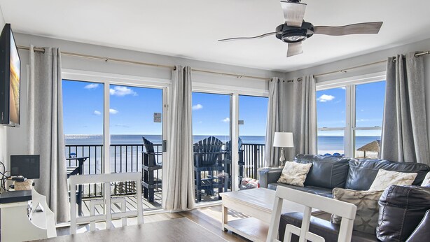 A spacious living room with a large window offering a view of the sea, a ceiling fan, and a seating area with a sofa and chairs. - Windancer 212. Gulf Front End Unit, Free Beach Service, Heated Pool. (Miramar Beach)
