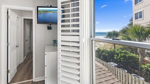 A room with a large window overlooking a beach, a television mounted on the wall, and a white door leading to another room. - Windancer 212. Gulf Front End Unit, Free Beach Service, Heated Pool. (Miramar Beach)
