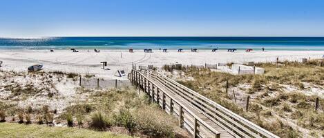 Een strand met een houten looppad dat naar de kust leidt, zandstrand en helderblauwe lucht.