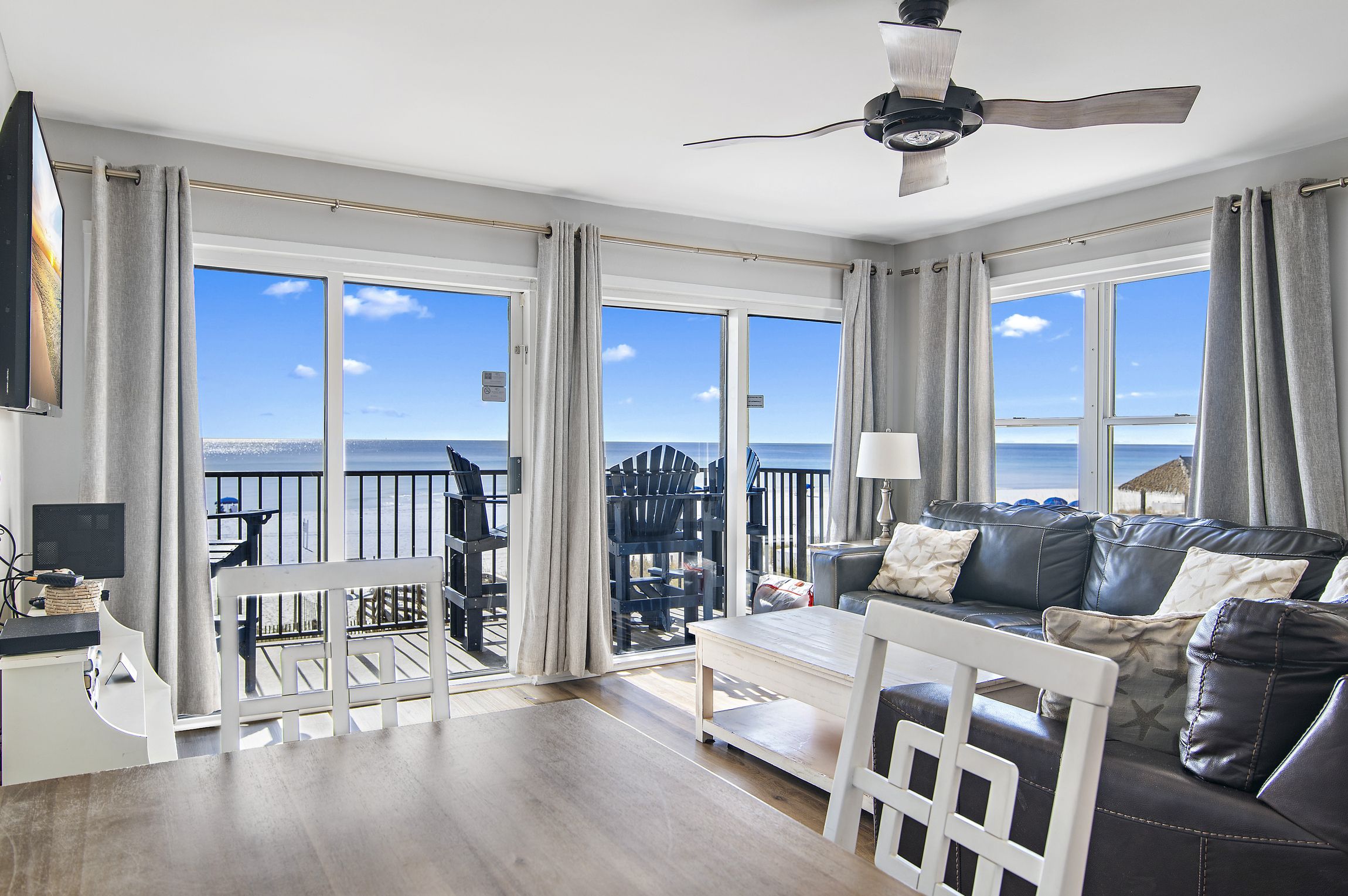 A spacious living room with a large window offering a view of the sea, a ceiling fan, and a seating area with a sofa and chairs.