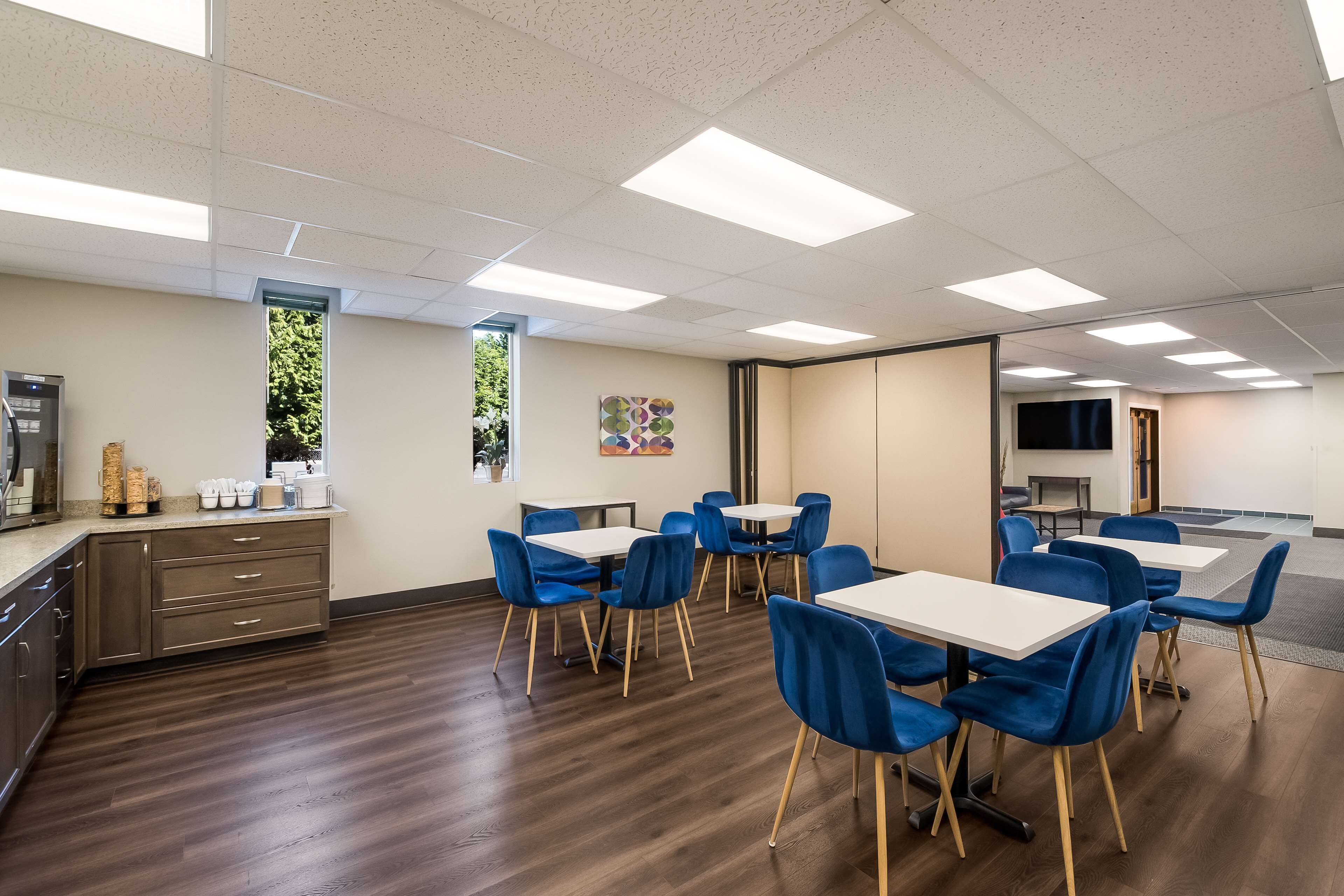 A modern conference room with wooden flooring, white tables, and blue chairs.