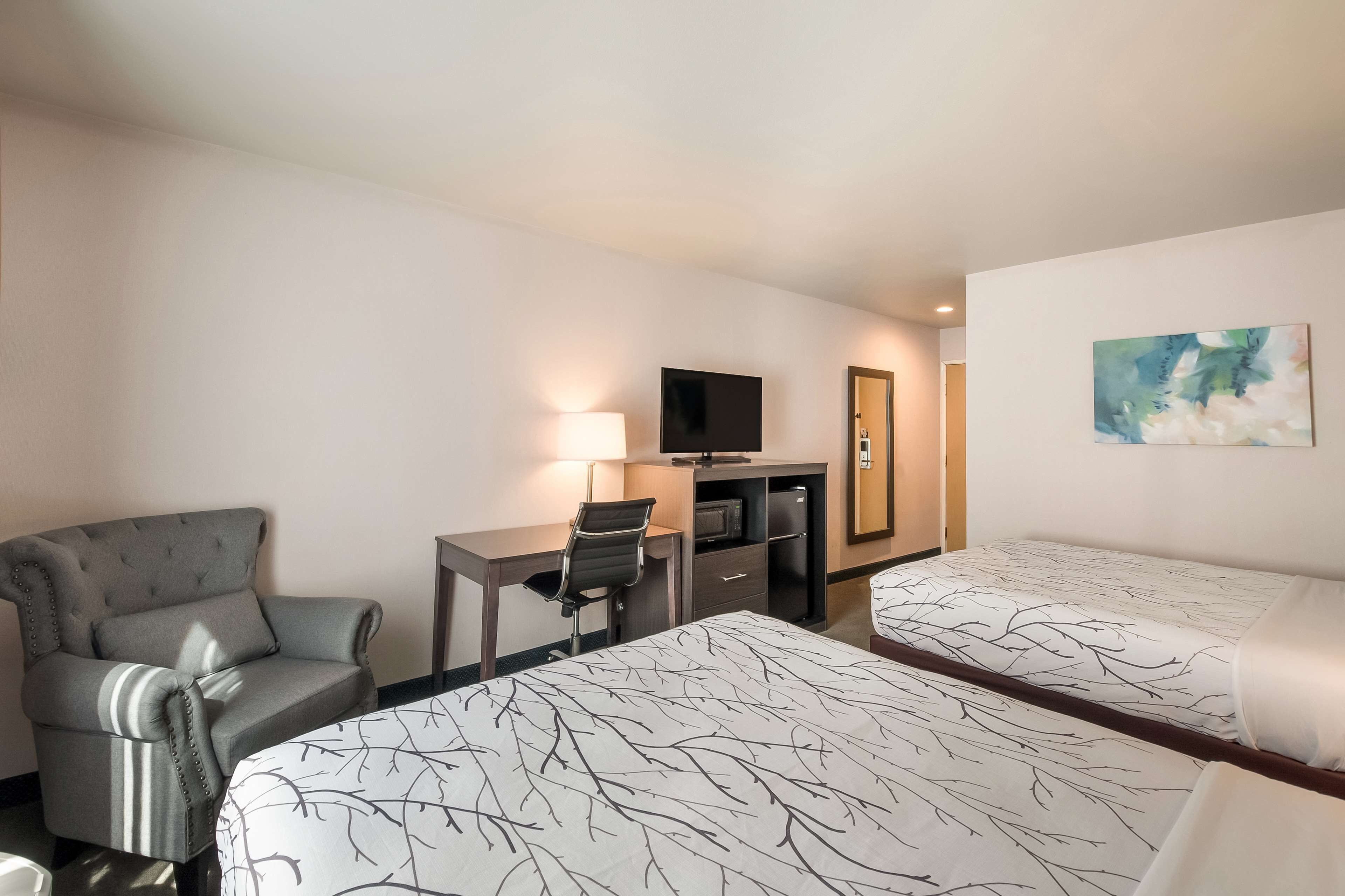 A hotel room with two beds, a desk with a chair, a television, and a painting on the wall.