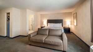 A hotel room with a bed, two bedside lamps, a sofa, a mirror, and a door leading to a bathroom.