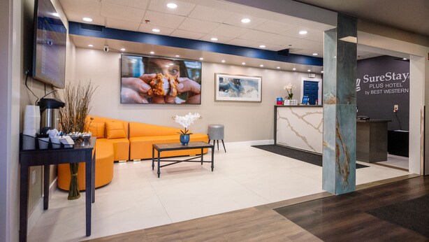 A hotel reception area with a modern design, including a reception desk, a seating area with an orange sofa, and a coffee table.