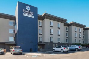 Ein mehrgeschossiges Hotel mit einem gut sichtbaren, blauen Schild für SureStay by Best Western. Es gibt mehrere Parkplätze, darunter Stellplätze für Menschen mit Behinderung.