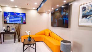 A modern living room with a sectional sofa, a coffee table, a round side table, and a flat-screen TV displaying flight information.