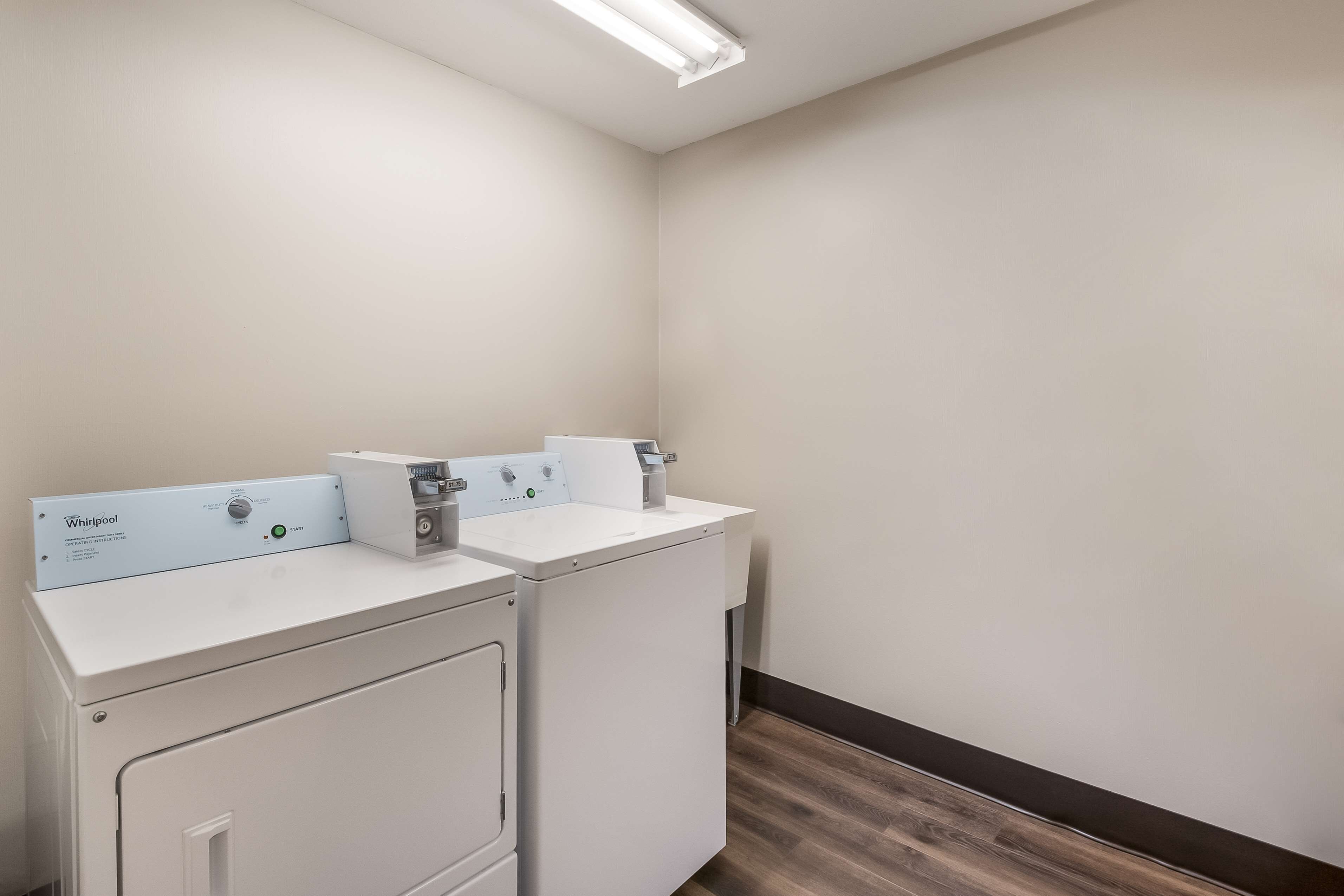 A laundry area with two white Whirlpool washers and dryers, a wooden floor, and a white wall.