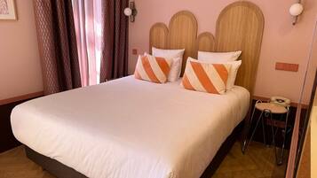 Una habitación de hotel con una cama grande, una mesita de noche con teléfono y una lámpara de pared.