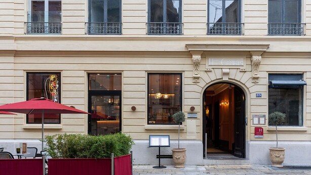 A building with a classic architectural style, featuring a central entrance with an arched doorway and a sign above it. There are multiple windows with black frames and a balcony with metal railings. - Hotel De Cambis (Avignon)