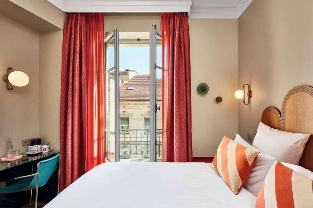 A hotel room with a bed, a desk with a telephone, and a view through a glass door.