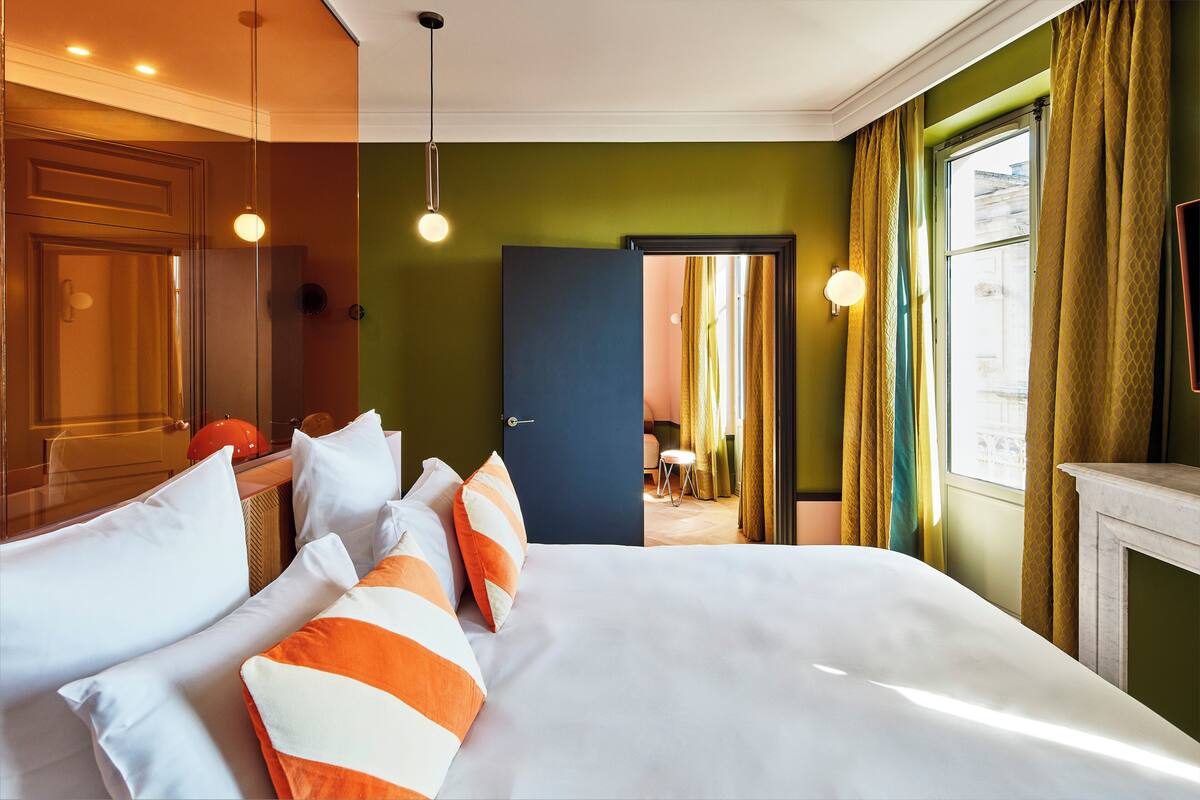 A hotel room with a bed, a desk, and a view of the city.