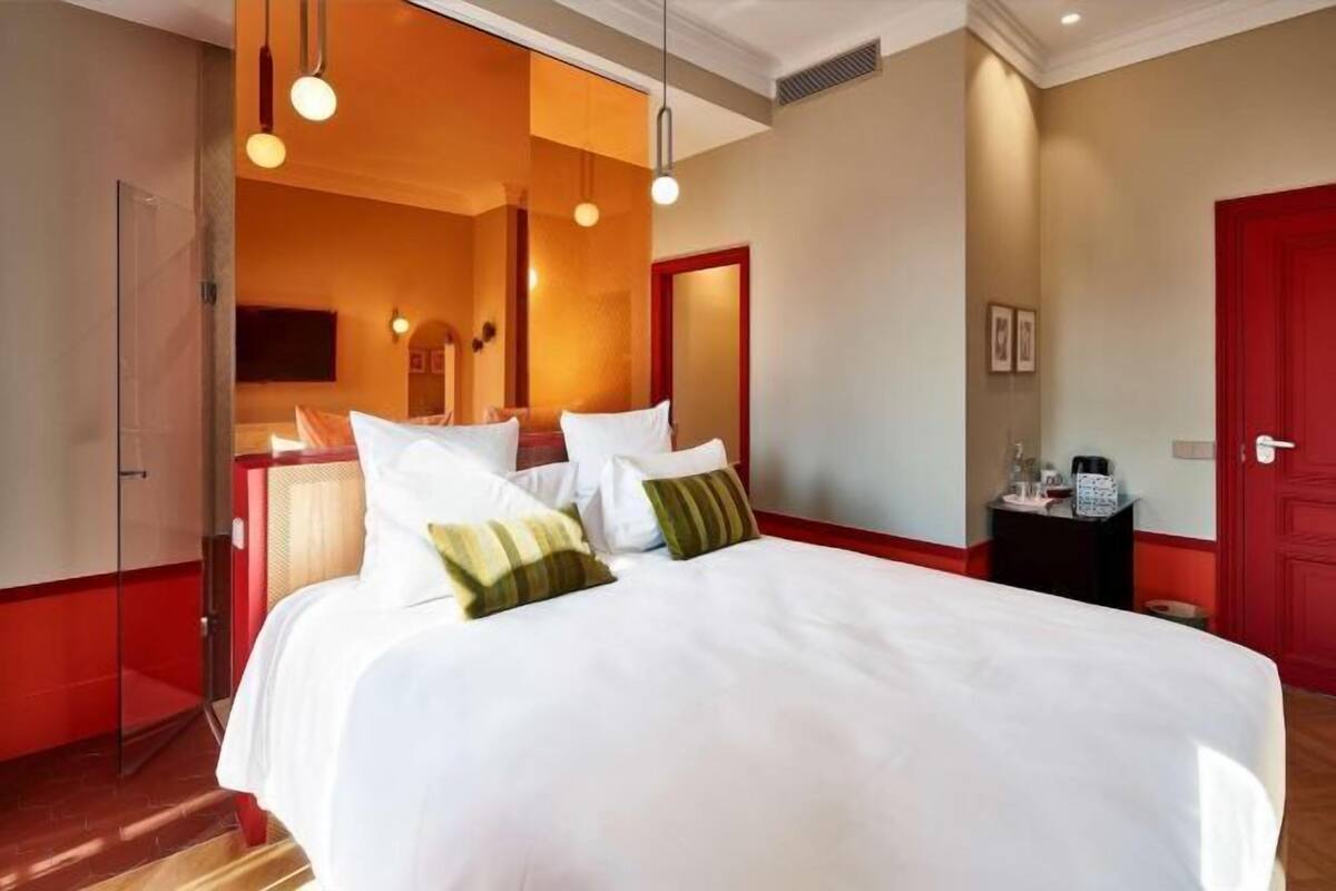 A hotel room with a large bed, a red door, and a mirror.