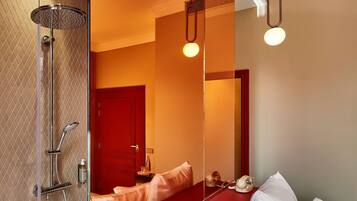 Une chambre d'hôtel moderne dotée d'une douche à parois de verre, d'un mur d'accent rouge, d'un grand miroir et d'un lit avec une literie blanche.