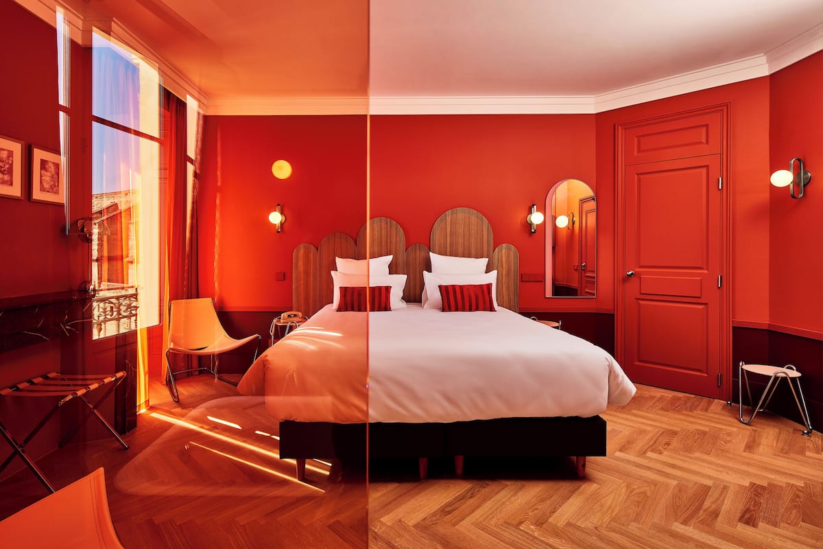 A room with a large bed, a chair, a lamp, and a door.