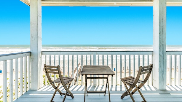 Una terraza de madera con dos sillas y una mesa, con vista a la playa.