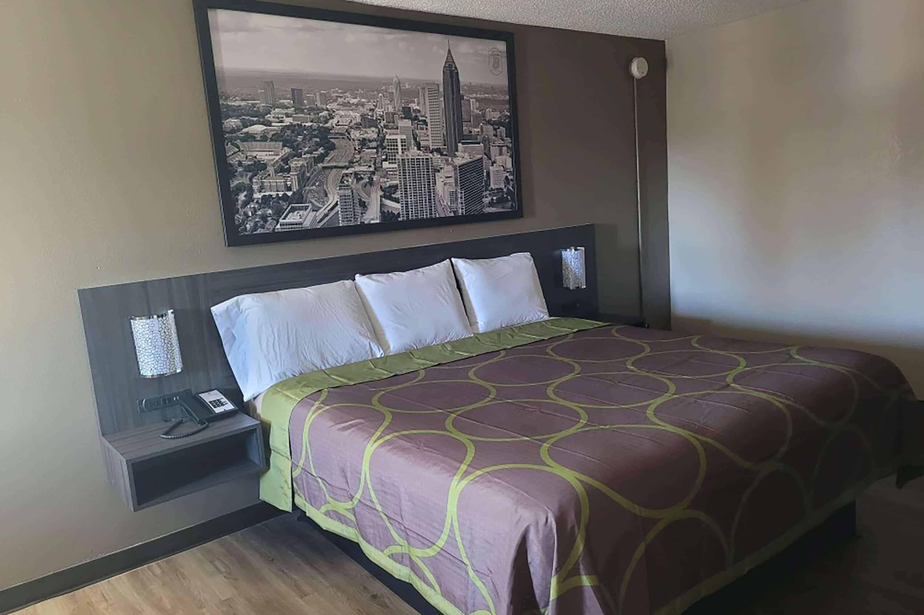 Ein Hotelzimmer mit einem Bett, einem Nachttisch, einem Telefon und einem Stadtbild an der Wand.