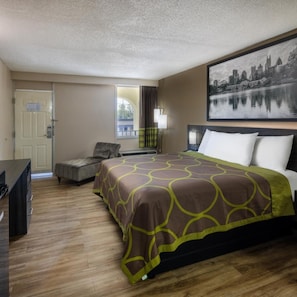 A hotel room with a bed, a desk, a chair, a window with a view, and a painting on the wall. - Super 8 by Wyndham Mcdonough GA (McDonough)
