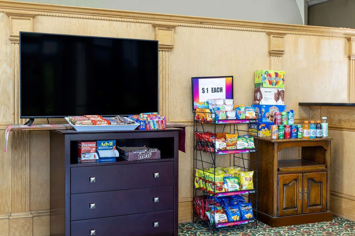 A hotel room with a TV on a stand, a snack display, and a small cabinet.