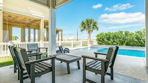 A covered outdoor seating area with a pool, wooden chairs, and a palm tree. - Beachside Home w/ POOL, 2 Covered Decks - 2 Blocks to Beach, 9 mi from Downtown (Galveston)
