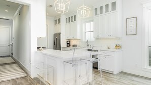 A modern kitchen with white cabinetry, a central island with bar stools, a stainless steel refrigerator, and pendant lighting. - Beachside Home w/ POOL, 2 Covered Decks - 2 Blocks to Beach, 9 mi from Downtown (Galveston)