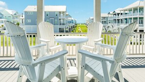 A deck with white Adirondack chairs and a small round table, overlooking a beachfront with multi-story buildings. - Beachside Home w/ POOL, 2 Covered Decks - 2 Blocks to Beach, 9 mi from Downtown (Galveston)
