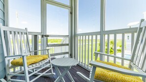 A porch with white wooden chairs and a small table, overlooking a green landscape. - Luxurious Beachside Home - All Suites, Large Living/Dining, Screened Porch (Galveston)