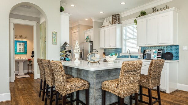 A kitchen with a central island, bar stools, white cabinets, and a blue-tiled backsplash. - Luxurious Beachside Home - All Suites, Large Living/Dining, Screened Porch (Galveston)