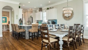 A spacious kitchen with white cabinets, a central island with bar stools, and a chandelier. - Luxurious Beachside Home - All Suites, Large Living/Dining, Screened Porch (Galveston)