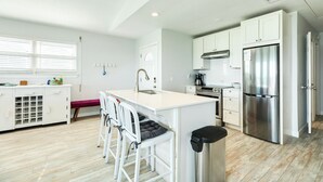 A modern kitchen with white cabinets, stainless steel appliances, and a central island with bar stools. - Updated Pet Friendly Beachfront Home w/ Open Plan, Equipped Kitchen, Free Wifi (Galveston)