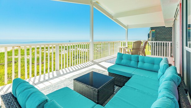 A covered outdoor seating area with a view of the ocean, a white railing, and a brick wall. - Updated Pet Friendly Beachfront Home w/ Open Plan, Equipped Kitchen, Free Wifi (Galveston)